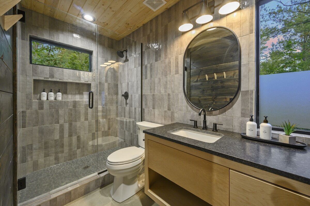 A modern bathroom with a large mirror, a toilet, a shower, and a sink.