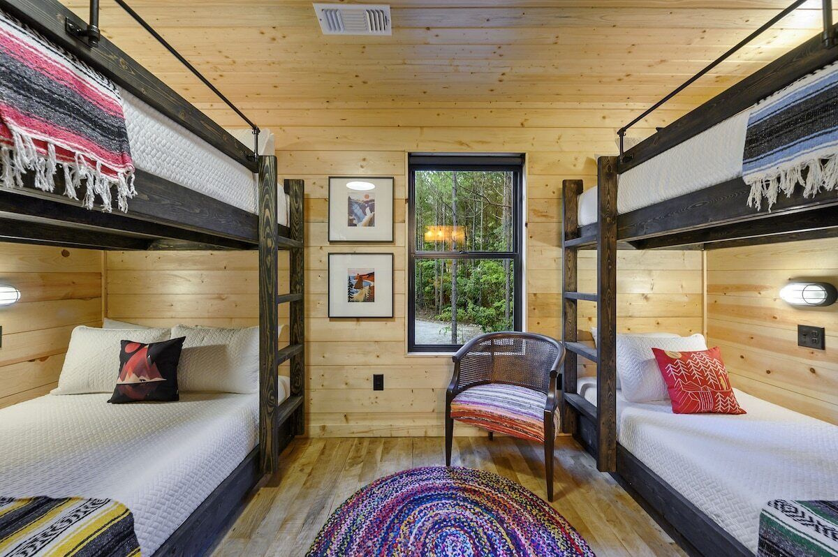 A cabin with two bunk beds, a rattan chair, and a window with a view of trees.
