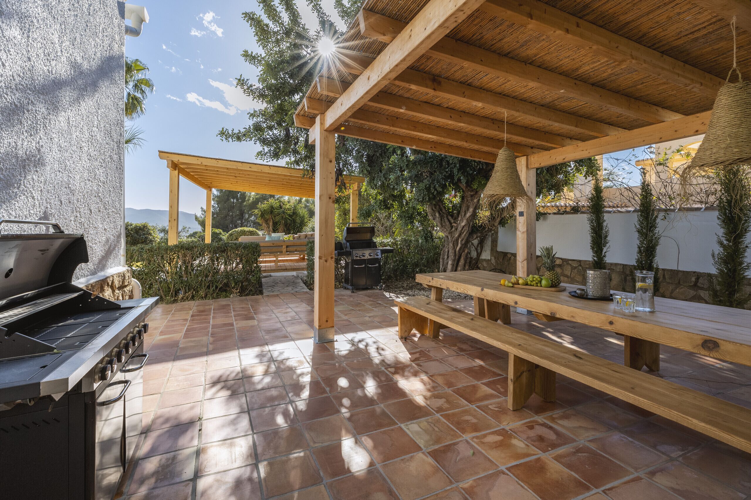 An outdoor patio with a grill, wooden benches, and a pergola.