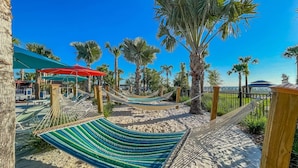 Een hangmat op een zandstrand, met palmbomen en een helderblauwe lucht op de achtergrond.