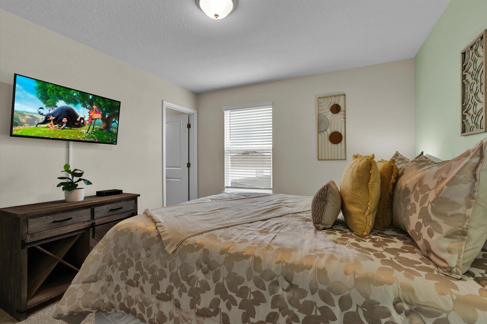 A bedroom with a bed, a TV, a dresser, a window with blinds, and a door.