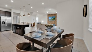 A modern kitchen with a central island, stainless steel appliances, pendant lighting, and a dining area with a wooden table set for four. - Windsor Island Resort 5 Bedroom Home Private Pool (Davenport)