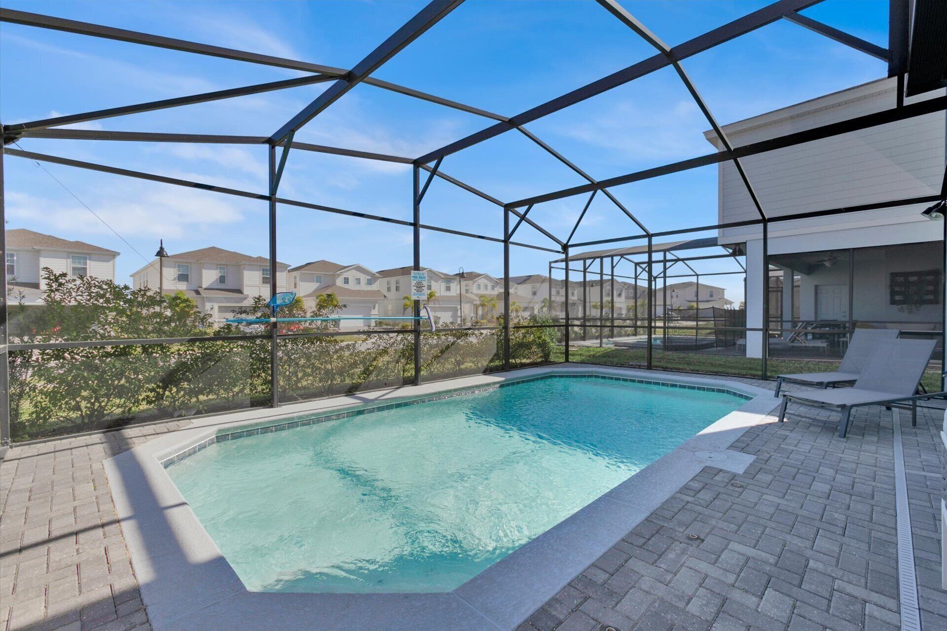 Une piscine à l’eau d’un bleu limpide, entourée d’une clôture en métal, et un espace patio aménagé avec des chaises.
