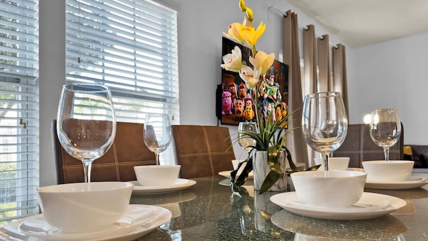 A dining table set with white bowls and wine glasses, a vase with yellow flowers, and a painting of animated characters in the background. - West Lucaya Village 4 Bedroom Townhome (Kissimmee)