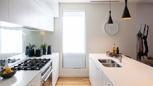 Una cocina moderna con armarios blancos, estufa a gas, pileta y luminarias colgantes.