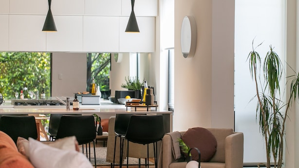 Una cocina moderna con comedor, una sala de estar con sofá y sillones, y un ventanal con vistas a la vegetación.