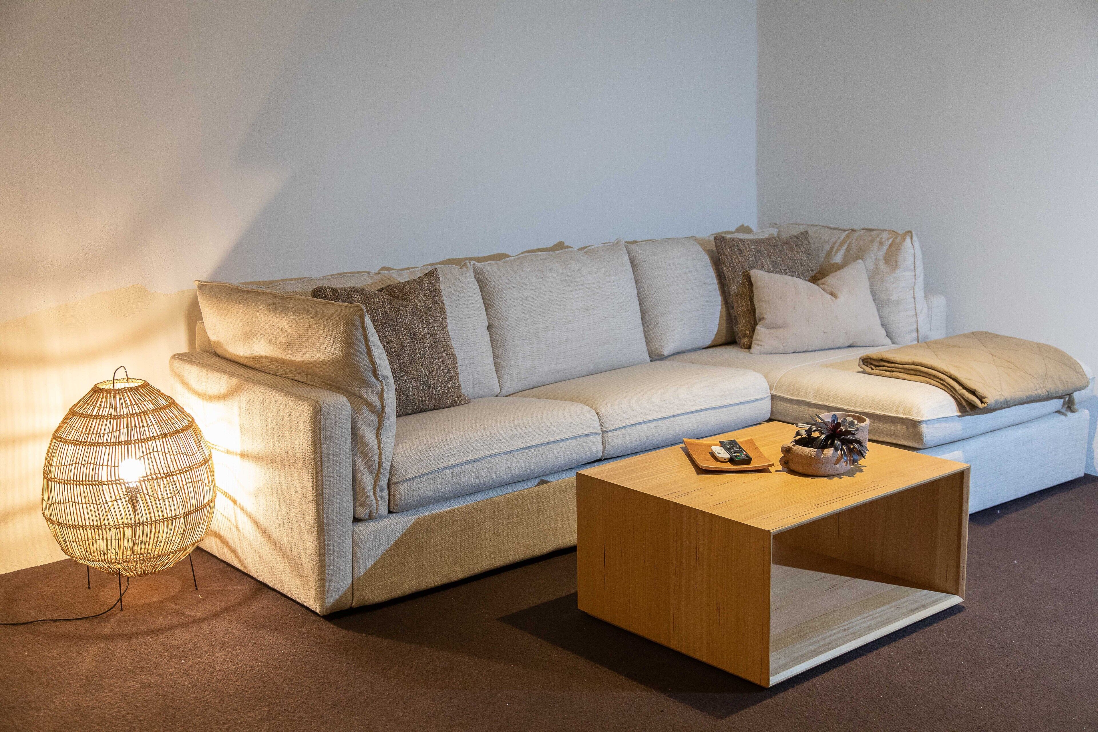 Ein modernes Wohnzimmer mit einem hellen Sofa, einem Holztisch und einer gewebten Stehlampe.