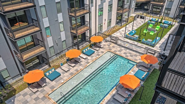 Un espace piscine aménagé sur le toit, doté de nombreuses chaises longues et de parasols, et entouré d’un immeuble de grande hauteur avec des balcons.
