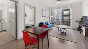 Un salon moderne comprenant un coin repas, un canapé bleu, un ventilateur de plafond et une vue sur un balcon.