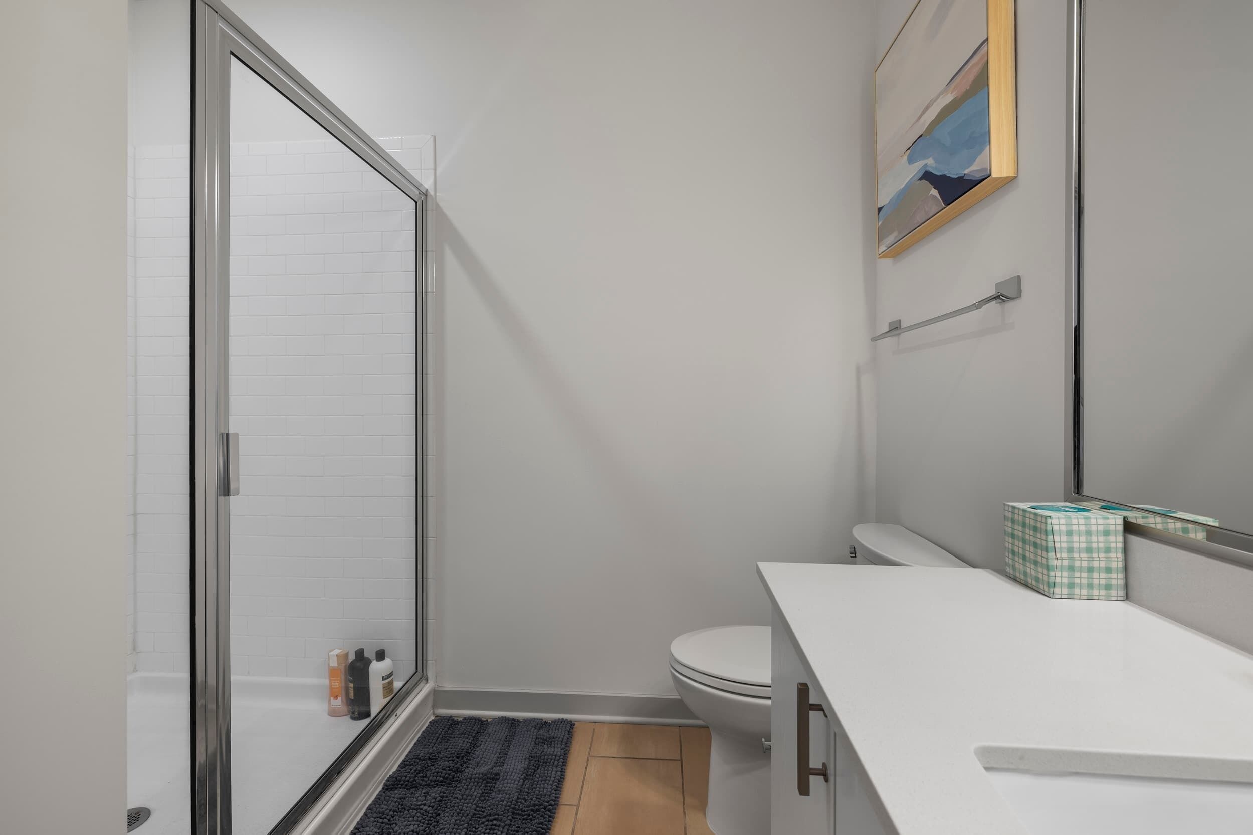 Et moderne badeværelse med en glasbrusekabine, et hvidt toilet og en hvid vask med et håndklædestativ.
