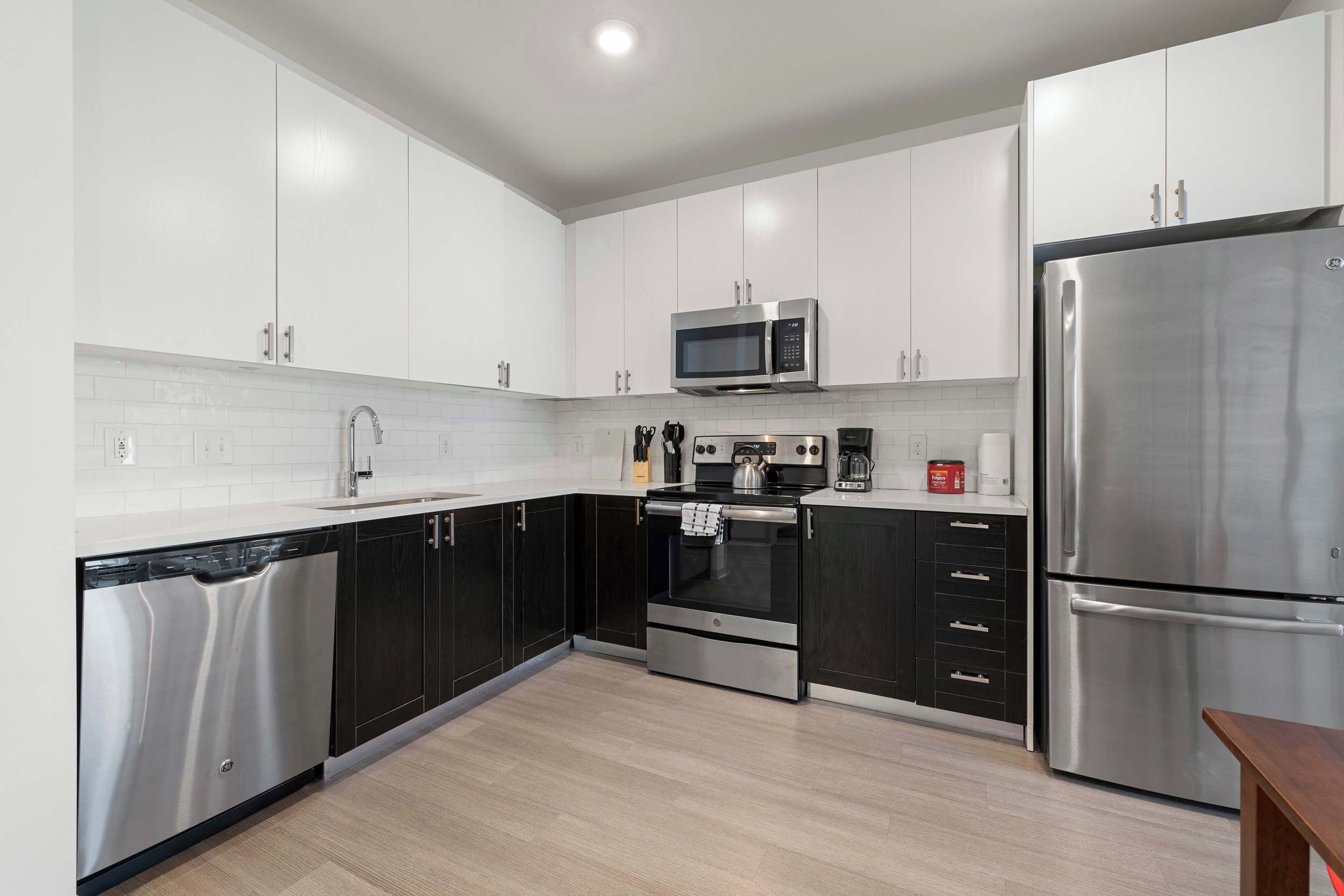 A modern kitchen with stainless steel appliances, white cabinetry, and a wooden floor.