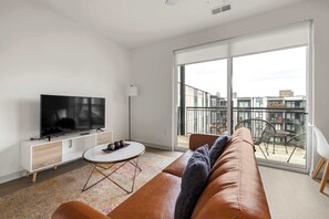 Ein modernes Wohnzimmer mit Flachbildfernseher, einer Couch, einem Couchtisch und einem Balkon mit Gartenmöbeln.