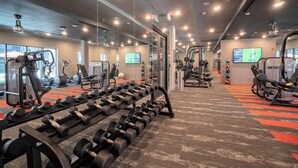 Une salle de sport équipée de matériel d’exercice, de miroirs et d’un écran de télévision.