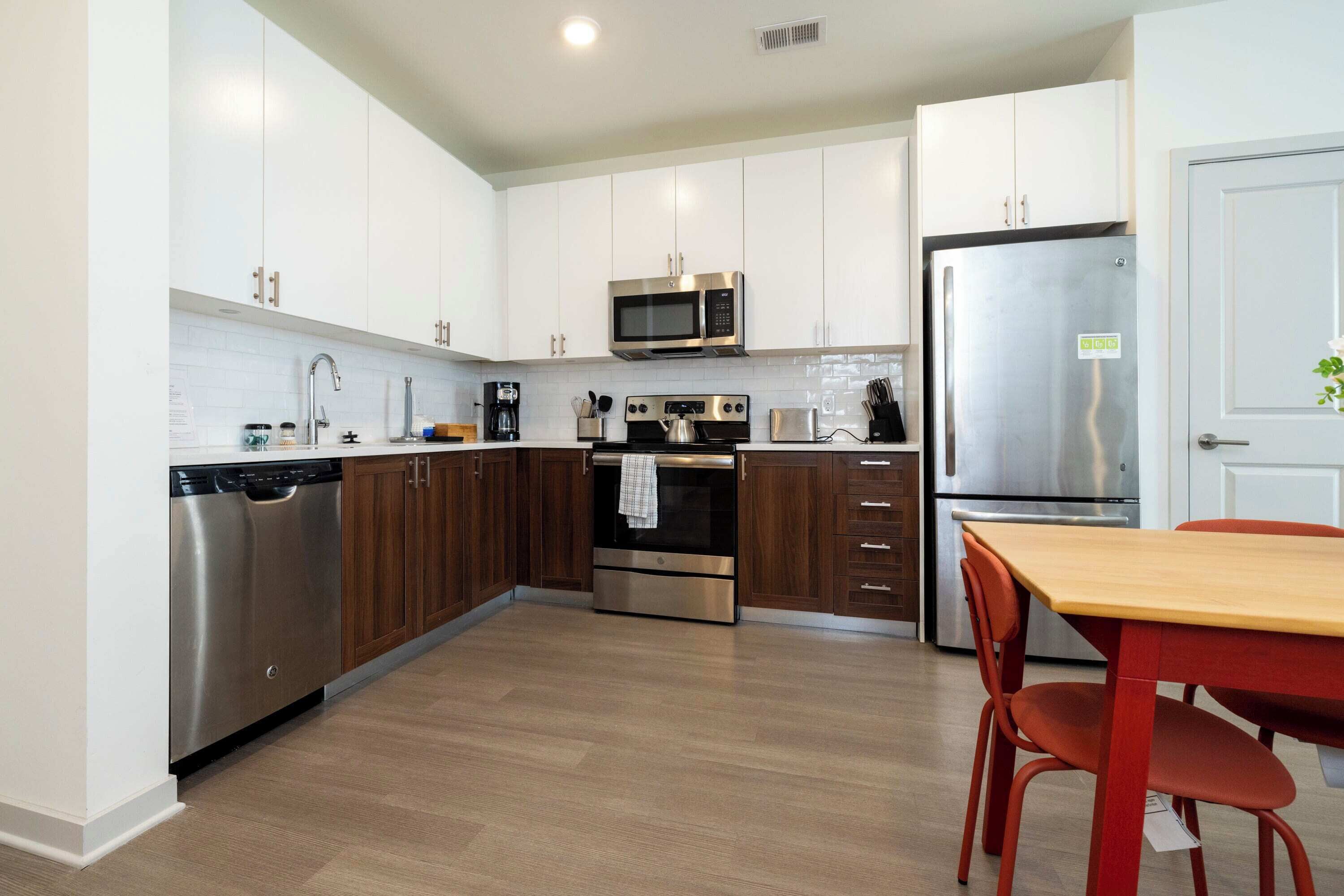 A modern kitchen with white cabinets, stainless steel appliances, and a wooden dining table.
