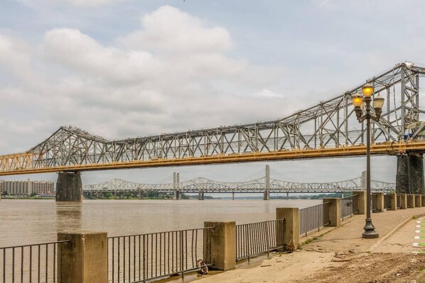 Eine große Stahlbrücke überspannt einen breiten Fluss, mit einem Fußweg und einer Straßenlaterne auf der rechten Seite.