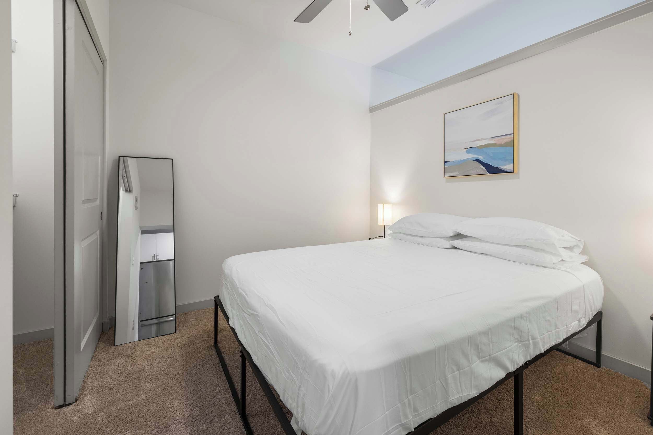 Ein Schlafzimmer mit einem Bett, einem Nachttisch, einem Wandbild und einer Tür.