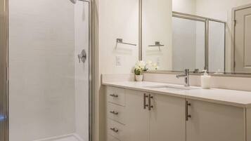 Un baño con cabina de ducha de vidrio, un lavabo con espejo y un mueble con cajones.