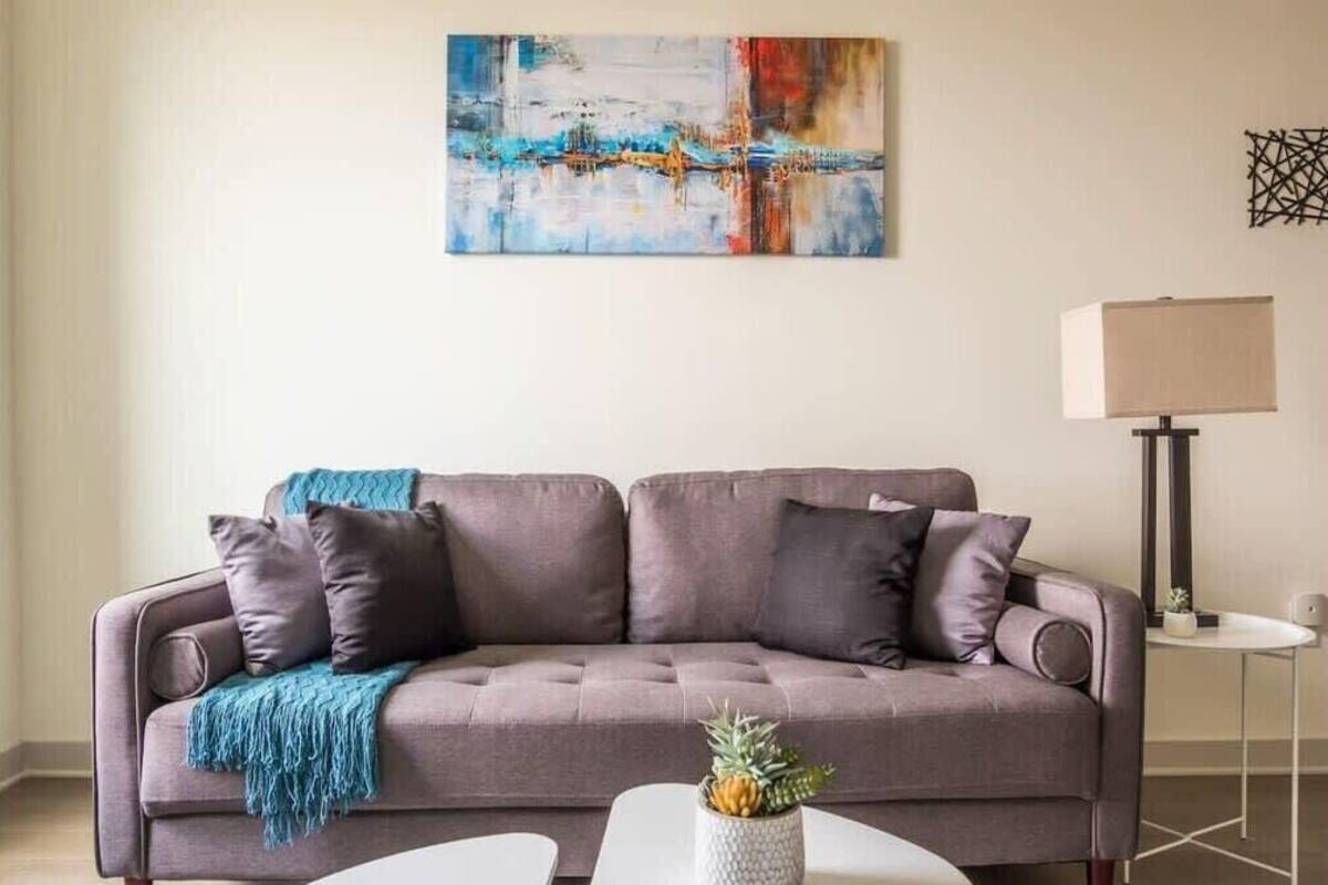 Un salon moderne avec un canapé gris, un plaid bleu et une petite table sur laquelle est posée une plante.