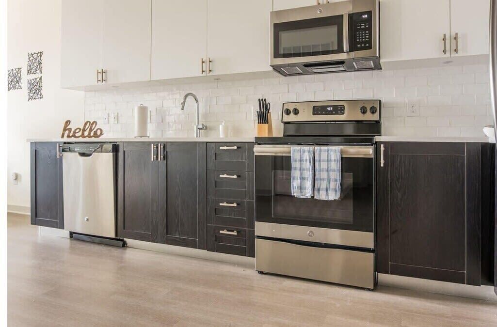 A modern kitchen with dark cabinets, stainless steel appliances, and a white tiled backsplash.
