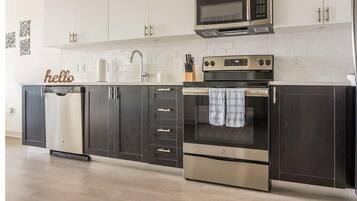A modern kitchen with dark cabinets, stainless steel appliances, and a white tiled backsplash.