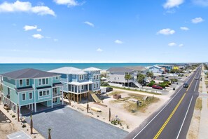 A coastal residential area with a two-story house featuring a balcony and a front porch. - "Dune Our Thing II" New Construction 8 Bedroom, 8 Bathroom Oceanfront Home w/ Pool! (Holden Beach)