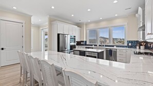 A modern kitchen with white cabinets, a large marble island, and a view of the neighborhood. - "Dune Our Thing II" New Construction 8 Bedroom, 8 Bathroom Oceanfront Home w/ Pool! (Holden Beach)