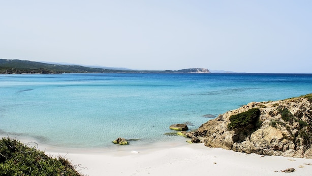 A coastal beach with clear turquoise waters, rocky shoreline, and distant hills. - Cottage with large outdoor space and A/C (Aglientu)