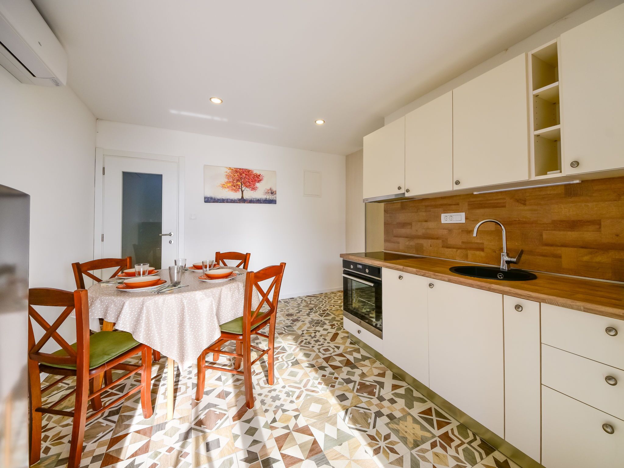 Una cocina moderna con encimera de madera, armarios blancos y suelo de baldosas estampadas.