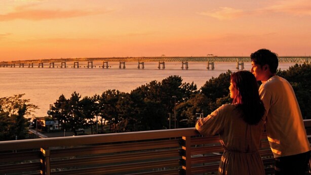 A couple on a bench overlooking a bridge and water during sunset. - EZ HOTEL KIX Seaside (Izumisano)