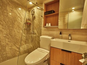 A modern bathroom with a marble wall, a toilet, a shower, and a wooden vanity with a mirror. - EZ HOTEL KIX Seaside (Izumisano)