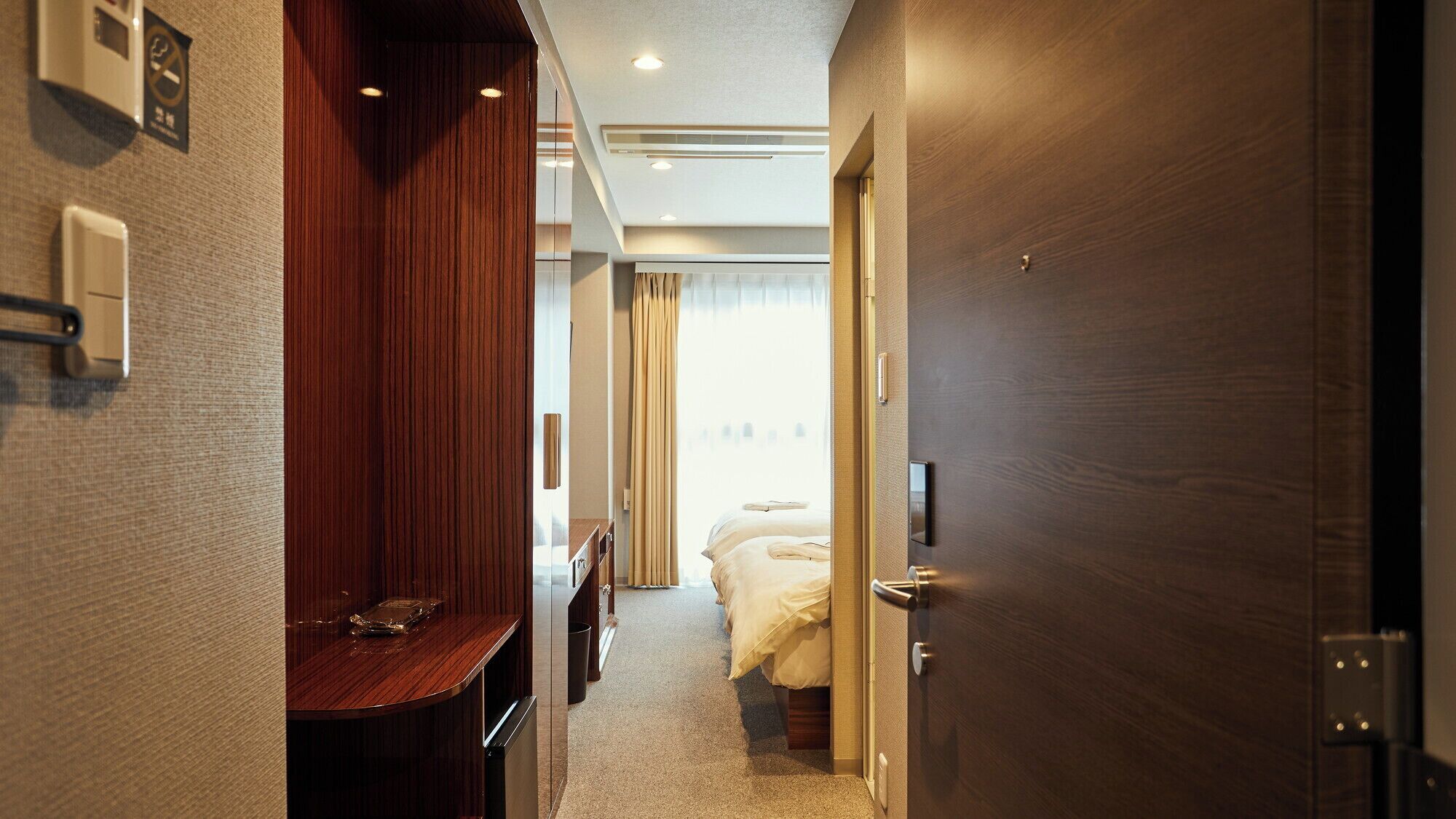 A hotel corridor with a wooden desk, a bed with white linens, and a door with a handle.