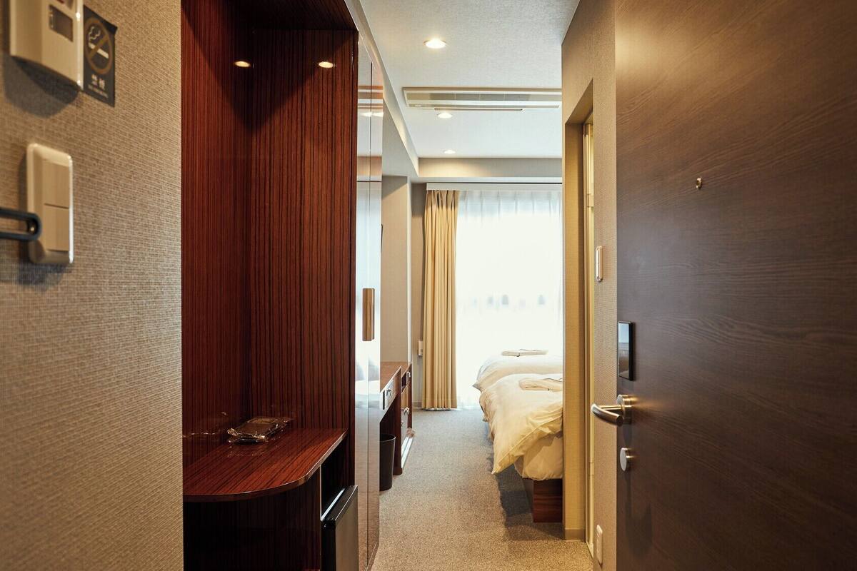 Ein Hotelkorridor mit einem Holztisch, einem Bett mit weißer Bettwäsche und einer Tür mit Griff.