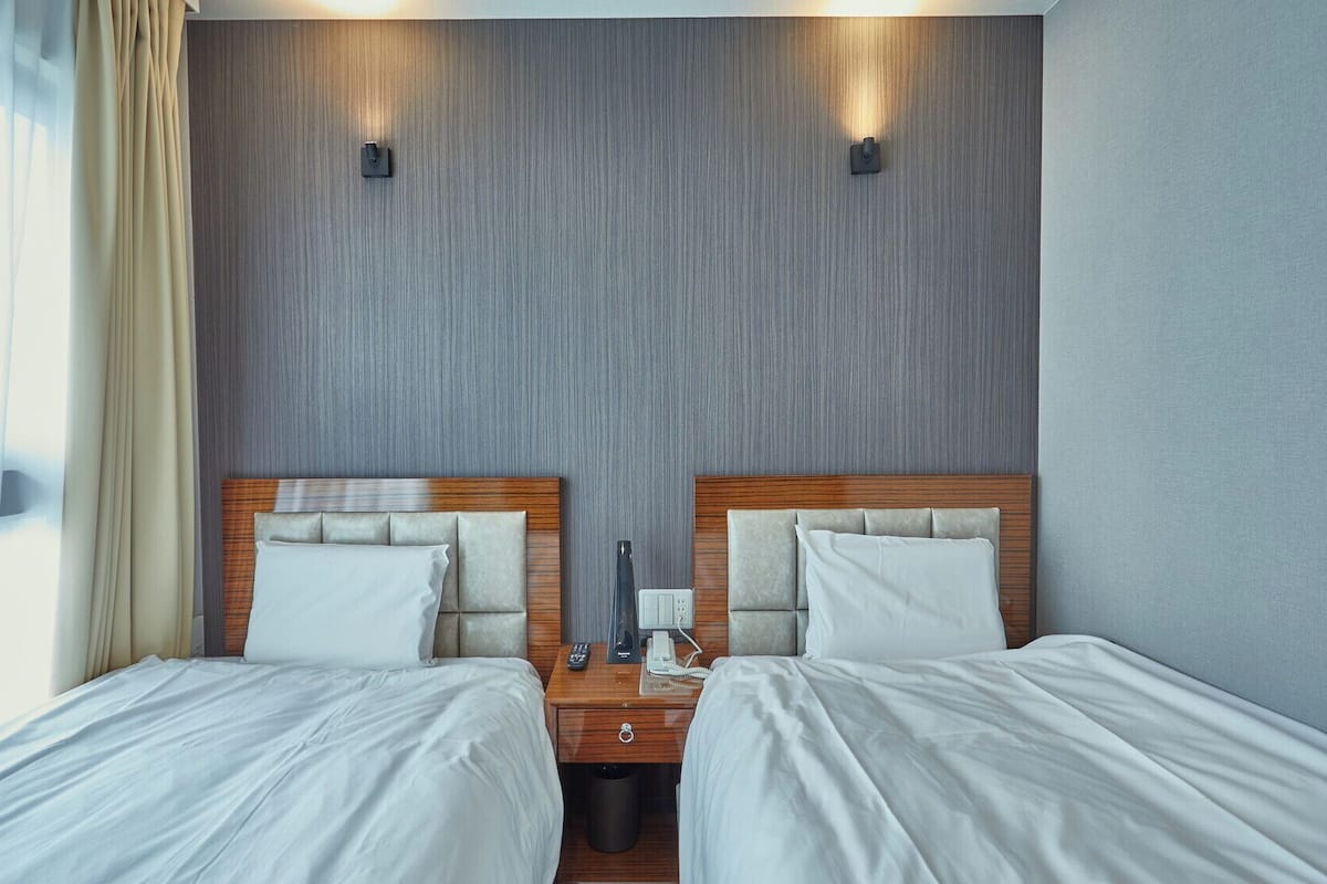Ein Hotelzimmer mit zwei Betten, einem Holznachttisch, einem Telefon und einer Wandleuchte.