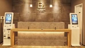 A reception desk with a digital kiosk on each side, a wooden reception counter, and a wall-mounted sign for EZ HOTEL. - EZ HOTEL KIX Seaside (Izumisano)
