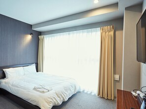 A modern hotel room with a neatly made bed, a large window with curtains, a flat-screen TV, and a small desk area. - EZ HOTEL KIX Seaside (Izumisano)