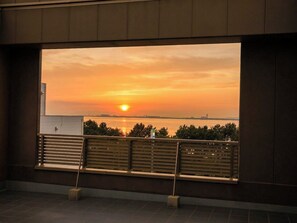 A sunset view from a balcony with a railing and a bench. - EZ HOTEL KIX Seaside (Izumisano)