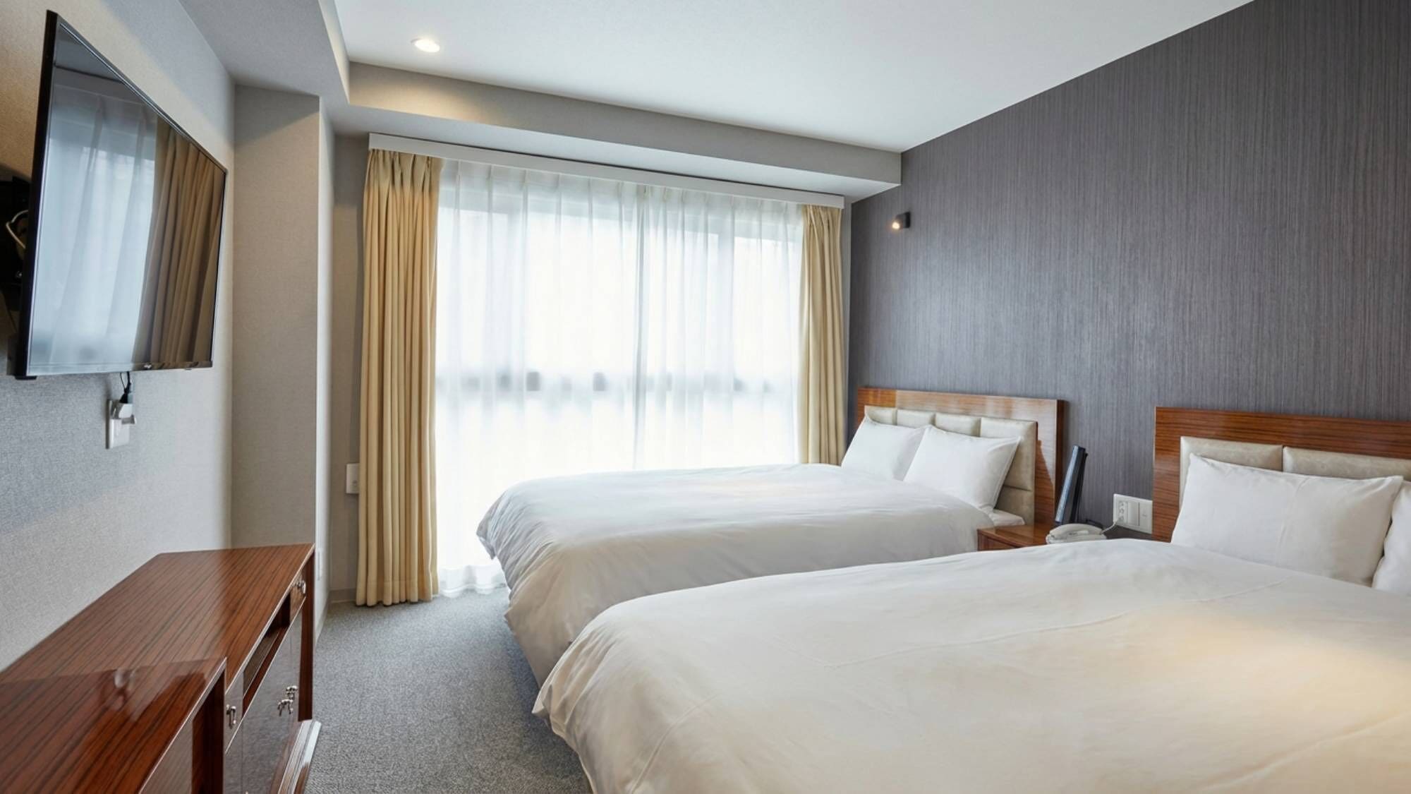 A hotel room with two beds, a TV, a desk, and a large window with curtains.