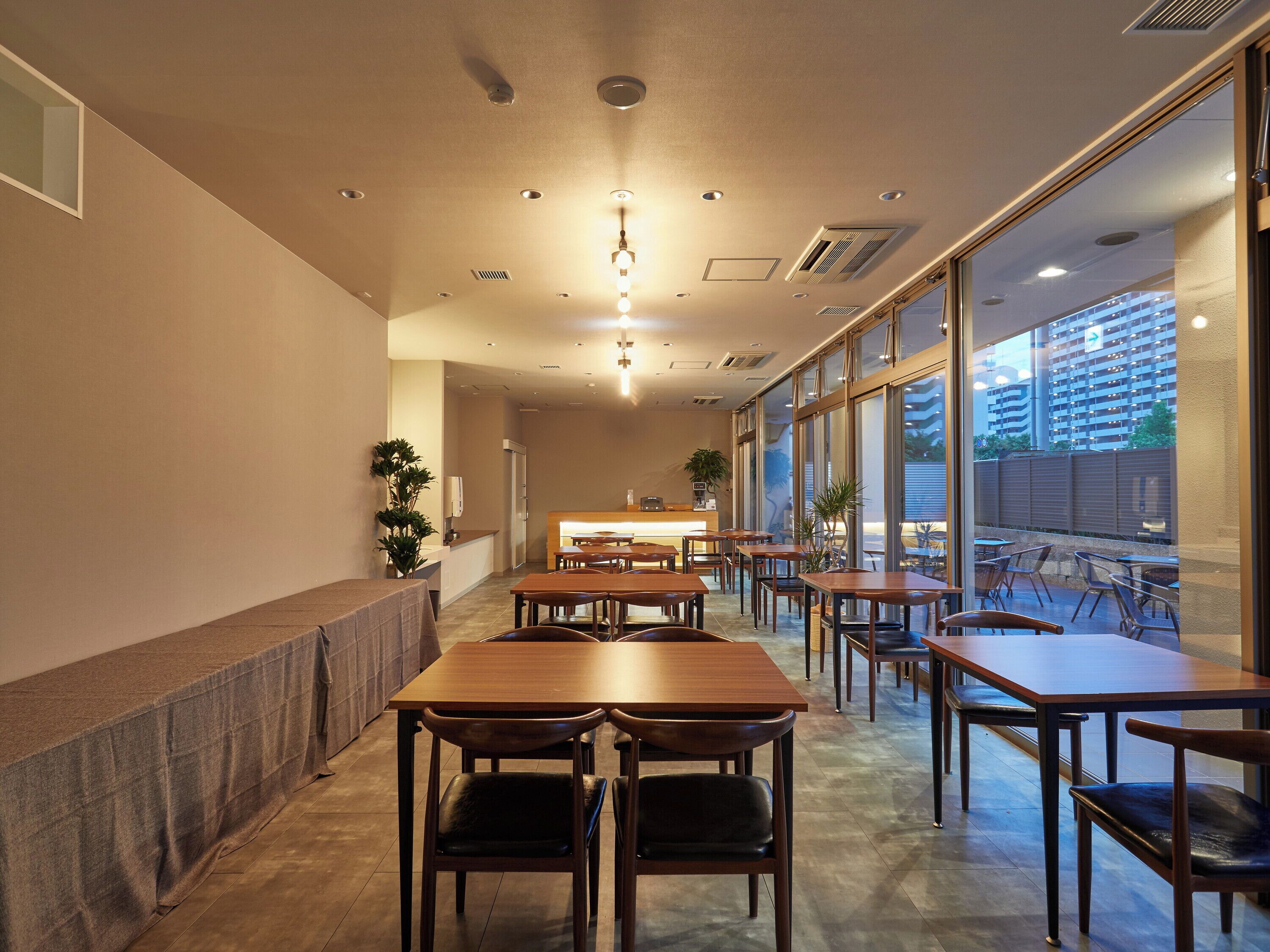 A modern restaurant interior with wooden tables and chairs, a reception desk, and large windows offering a view of the cityscape.