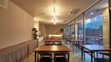 Interior moderno de restaurante com mesas e cadeiras de madeira, balcão de recepção e grandes janelas com vista para a paisagem urbana.
