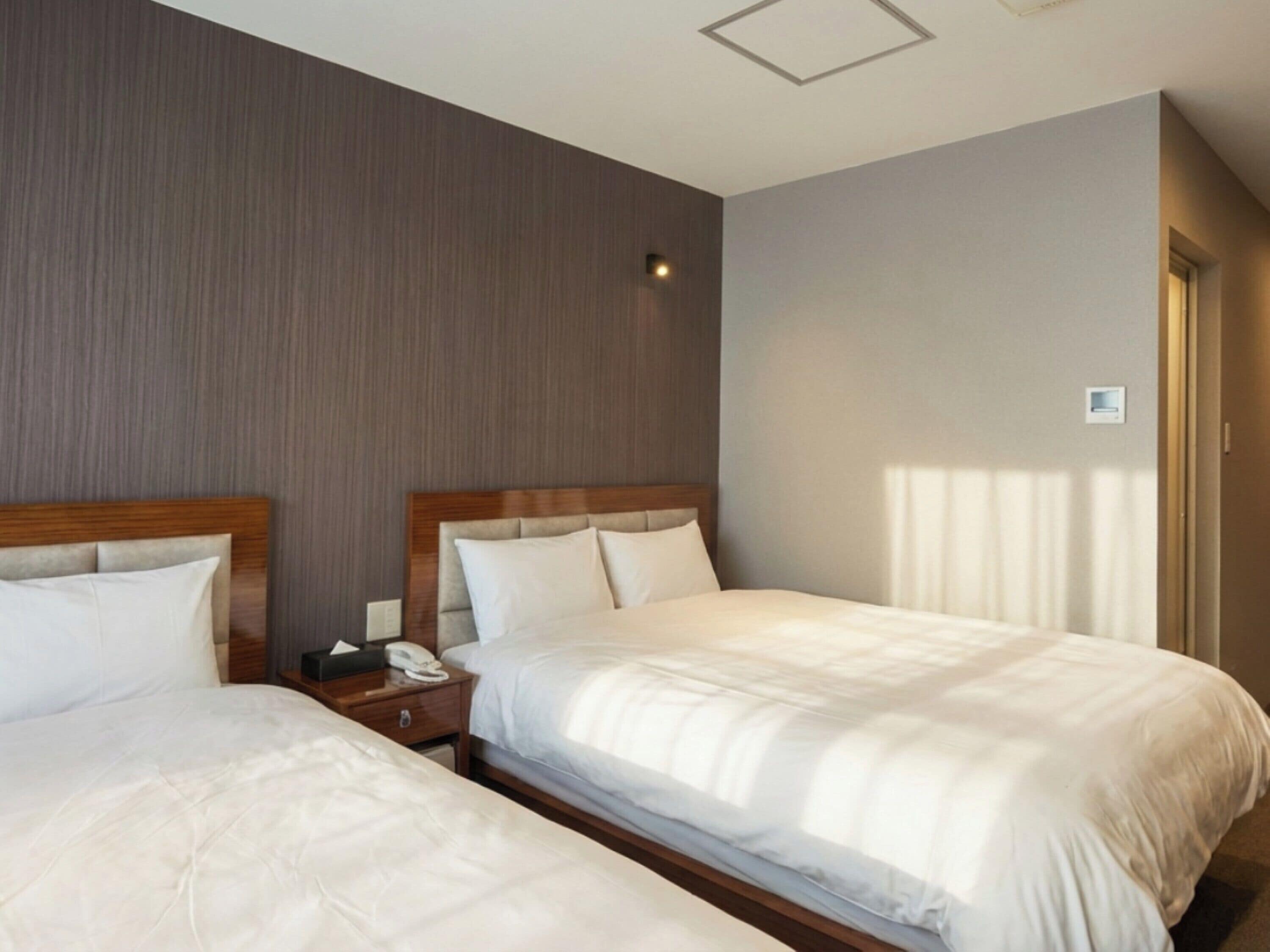Habitación de hotel con dos camas, cabeceros de madera, una mesita de noche con teléfono y una lámpara fijada a la pared.