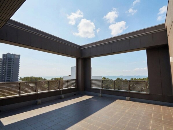 A spacious balcony with a clear view of the city skyline and a body of water in the distance. - EZ HOTEL KIX Seaside (Izumisano)