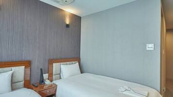 Habitació d'hotel amb dos llits, una taula de nit amb un telèfon i un comandament a distància, i un aire condicionat fixat a la paret.