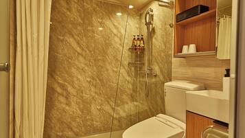 Un baño con pared de mármol, ducha, inodoro y repisa de madera con artículos de aseo.
