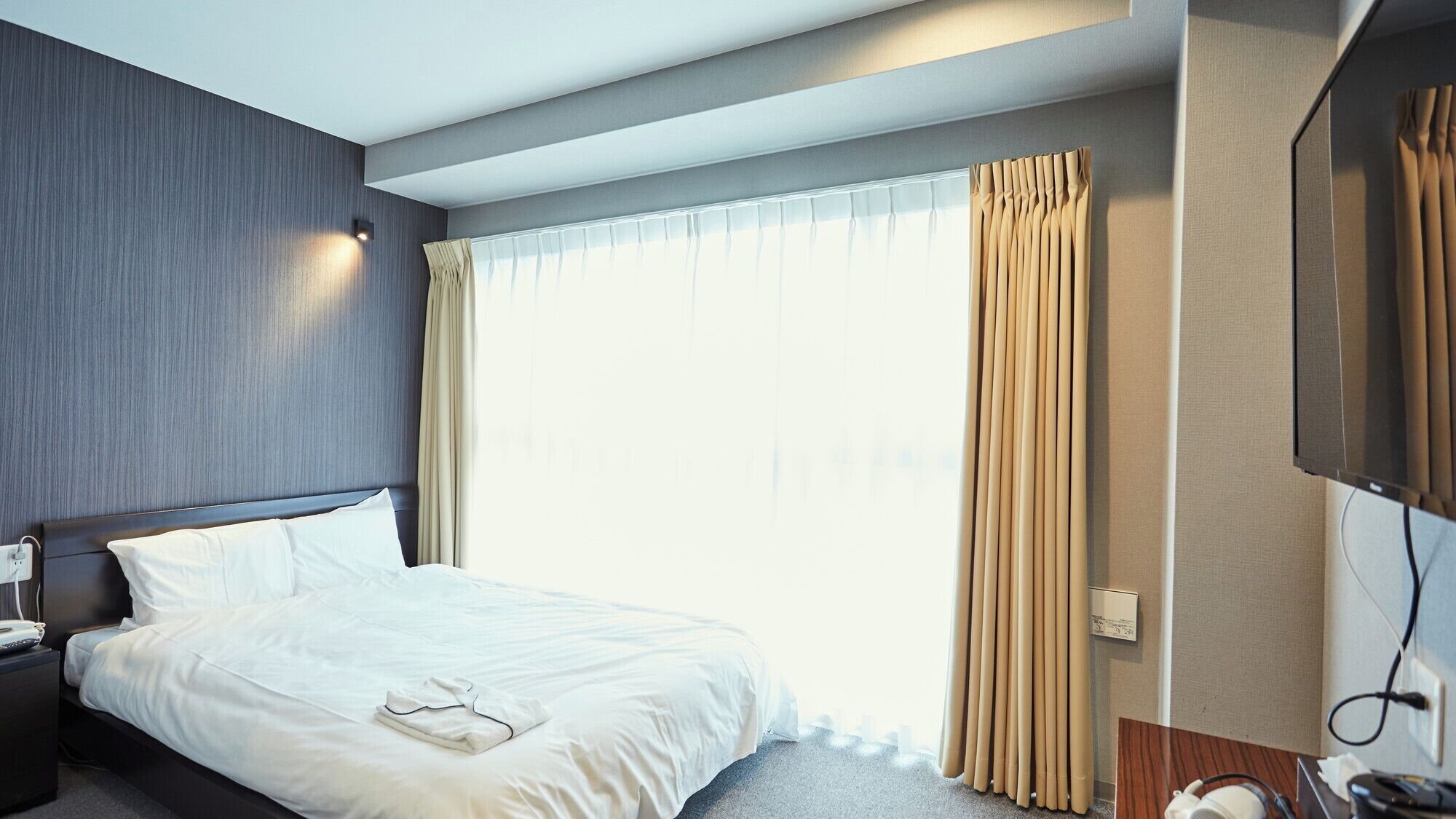 A hotel room with a bed, bedside table, TV, and curtains.
