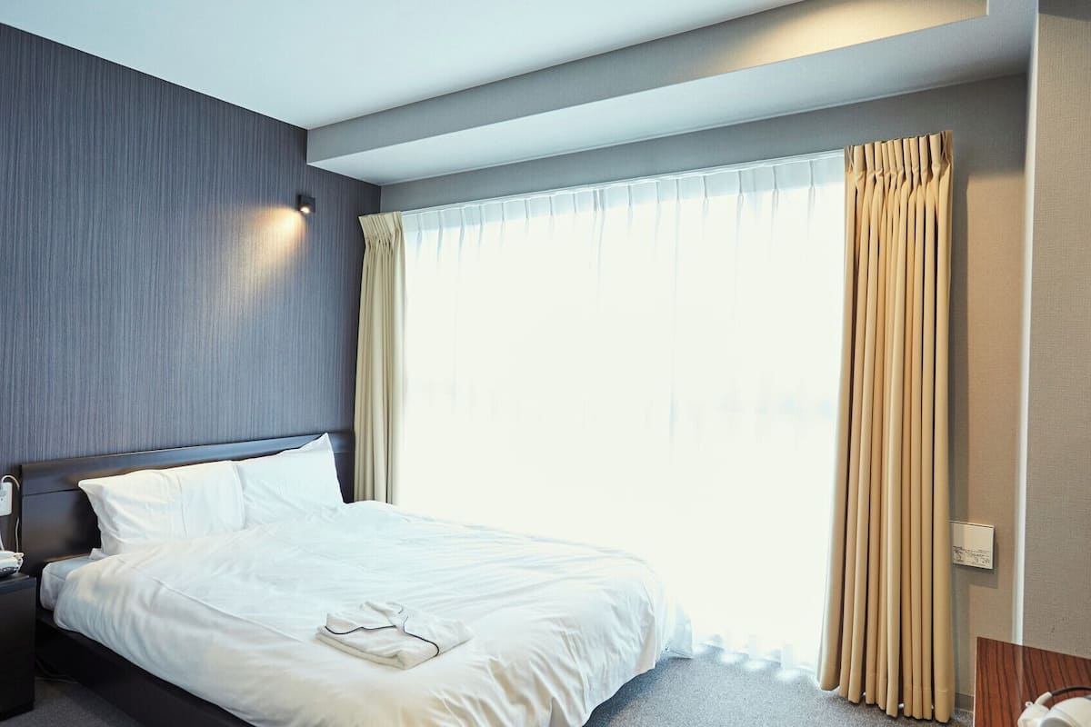 Ein Hotelzimmer mit Bett, Nachttisch, Fernseher und Vorhängen.