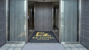 The entrance to a hotel with a modern design, featuring a glass door and a black mat with the hotel name. - EZ HOTEL KIX Seaside (Izumisano)