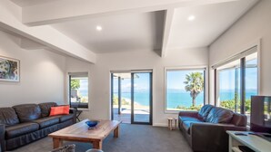 Een moderne woonkamer met een bank, een salontafel en een tv-meubel. Grote ramen bieden uitzicht op de zee.