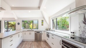 Een moderne keuken met witte kasten, roestvrijstalen apparatuur en grote ramen met uitzicht op groen.