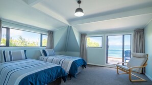 Een slaapkamer met twee bedden, een stoel en grote ramen met uitzicht op zee.