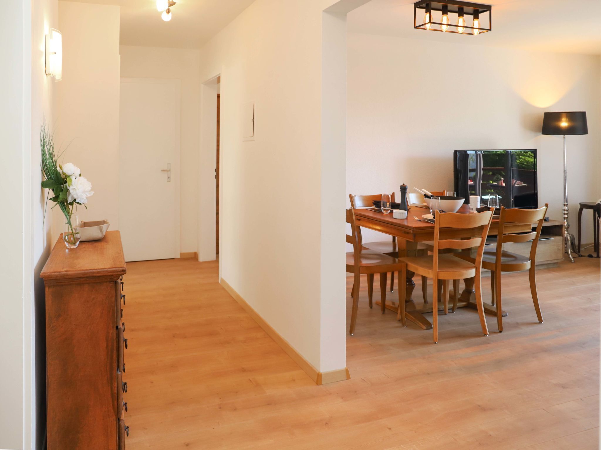 Un coin repas avec une table et des chaises en bois, un téléviseur et une lampe.
